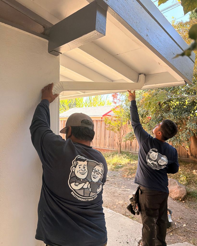 Two crew members working a downspout under the eave