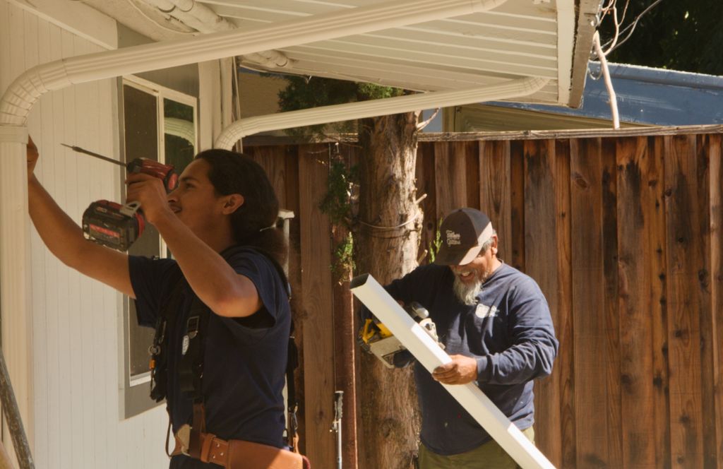 Fastening a downspout while a teammate brings the next section