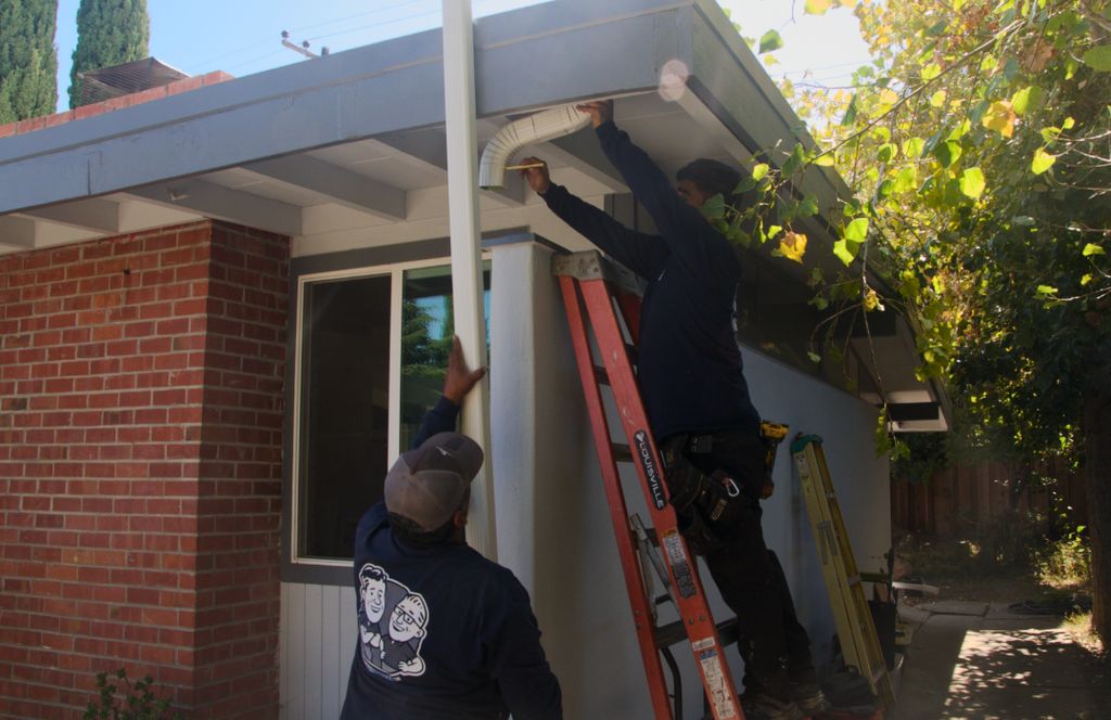 Two crew members hanging a new downspout on a brick ranch home