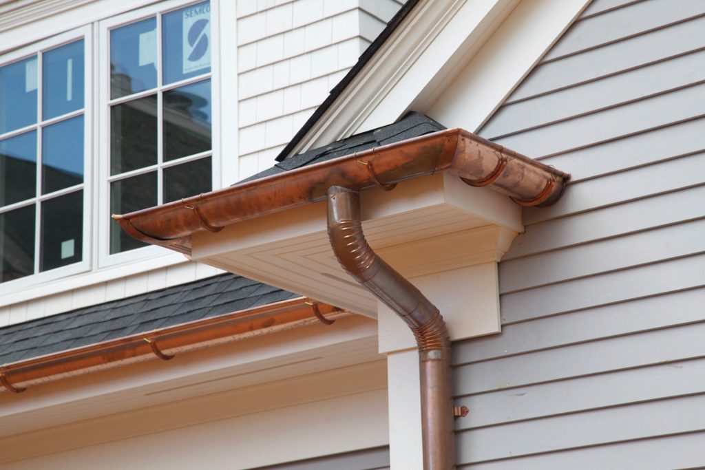 A copper downspout and gutter on white siding
