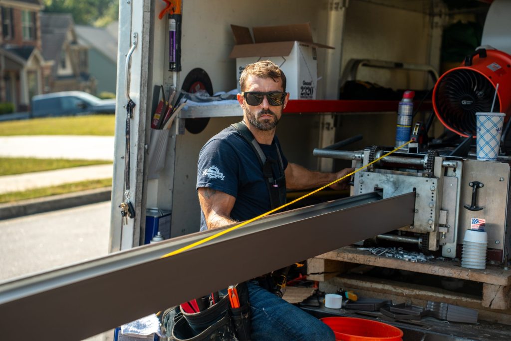 Crew member feeding a dark seamless gutter run out of the gutter machine in the back of the work truck