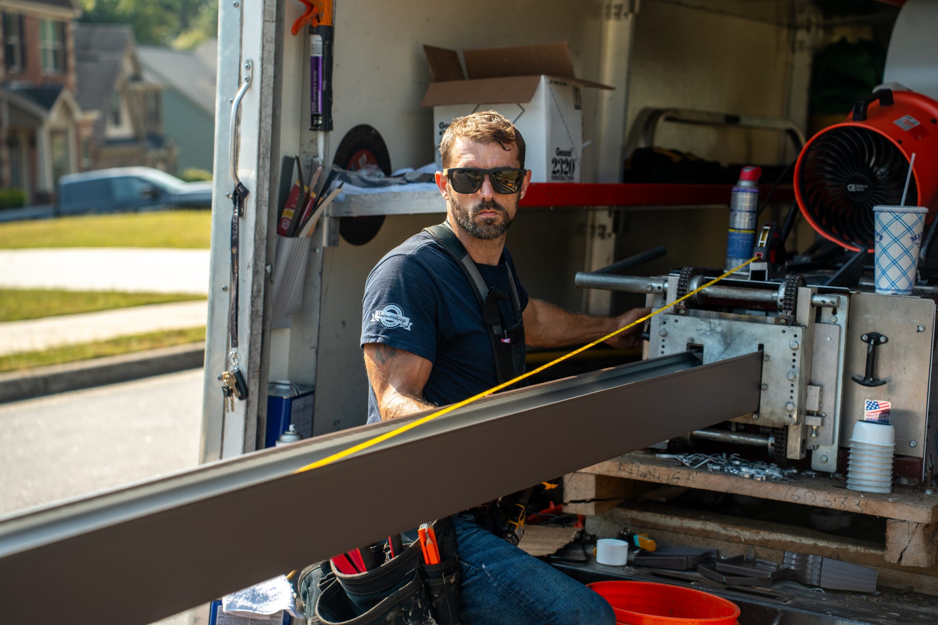 Crew member feeding a dark seamless gutter run out of the gutter machine in the back of the work truck